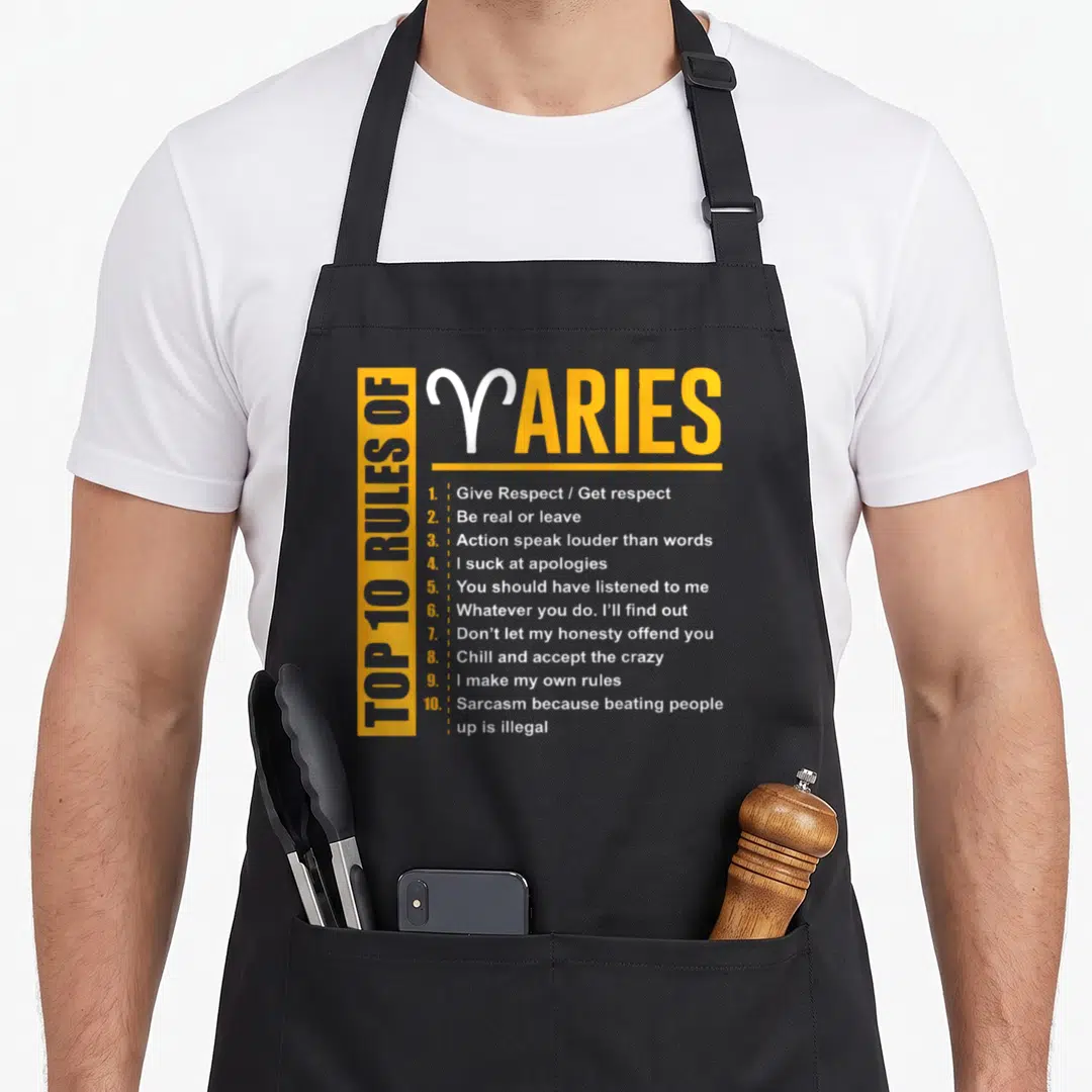 Birthday aries kitchen apron - Yellow and white typography listing ten Aries rules including sarcasm and honesty — shown on a black cotton canvas apron against a white background