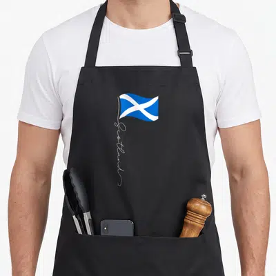 Scotland patriotic apron - Blue and white flag with vertical white script reading Scotland on grey background — shown on a black cotton canvas apron against a white background