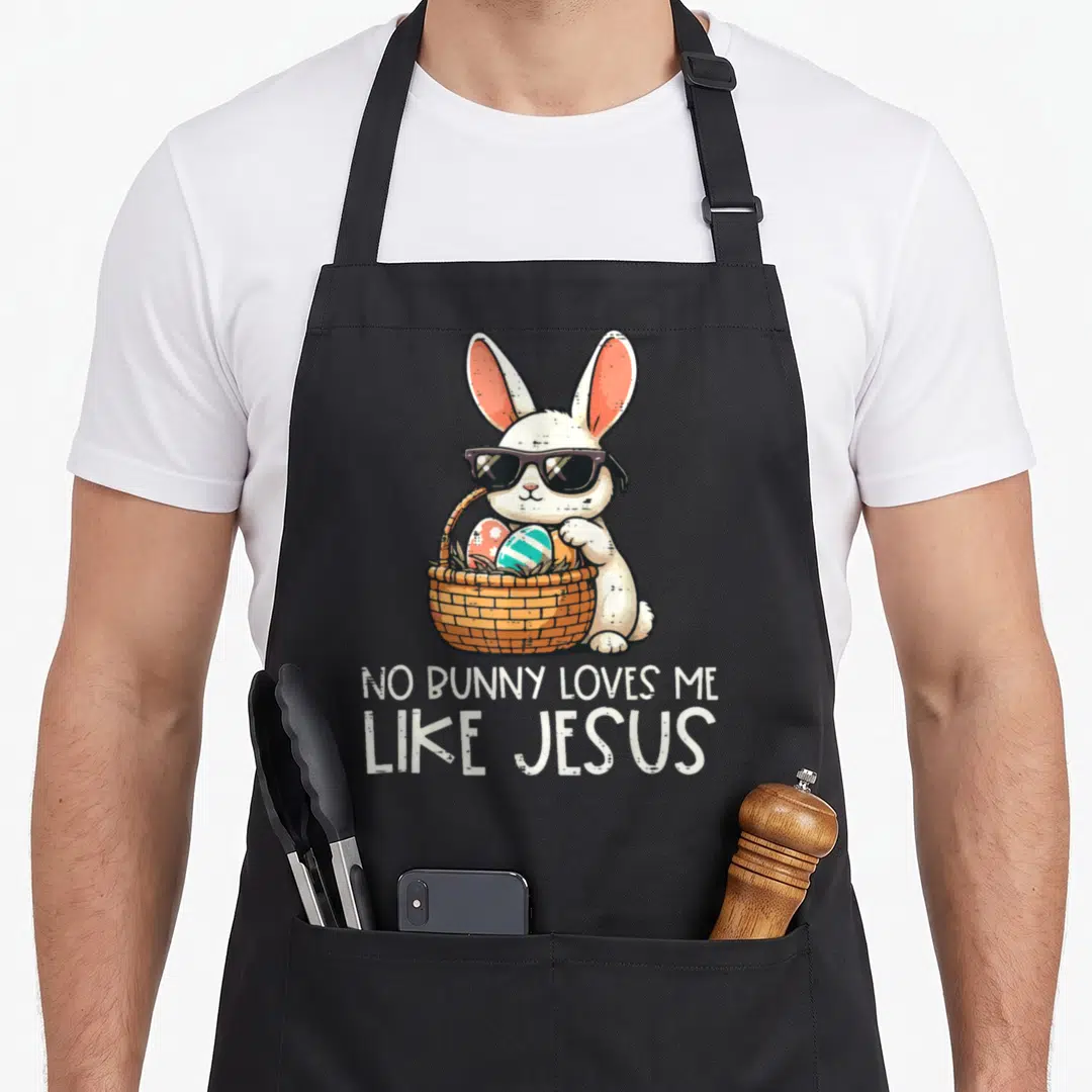 Jesus easter apron - Cartoon bunny with sunglasses holds basket of blue green red and white eggs under text NO BUNNY — shown on a black cotton canvas apron against a white background