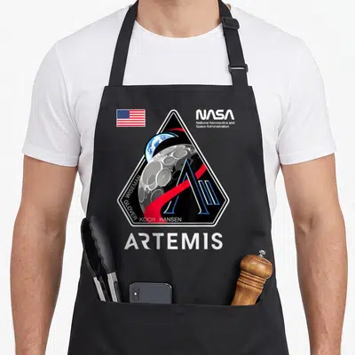 Patch nasa apron - Artemis mission patch with Earth moon NASA logo USA flag crew names ARTEMIS text — shown on a black cotton canvas apron against a white background