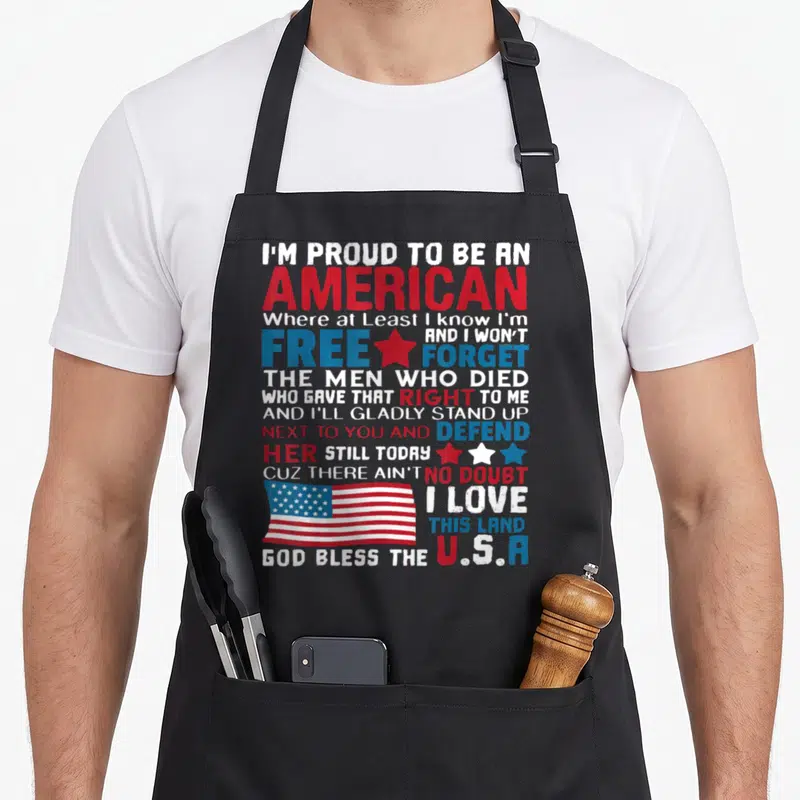 Featuring american flag apron - Stacked patriotic quote with USA flag and red white blue distressed text — shown on a black cotton canvas apron against a white background