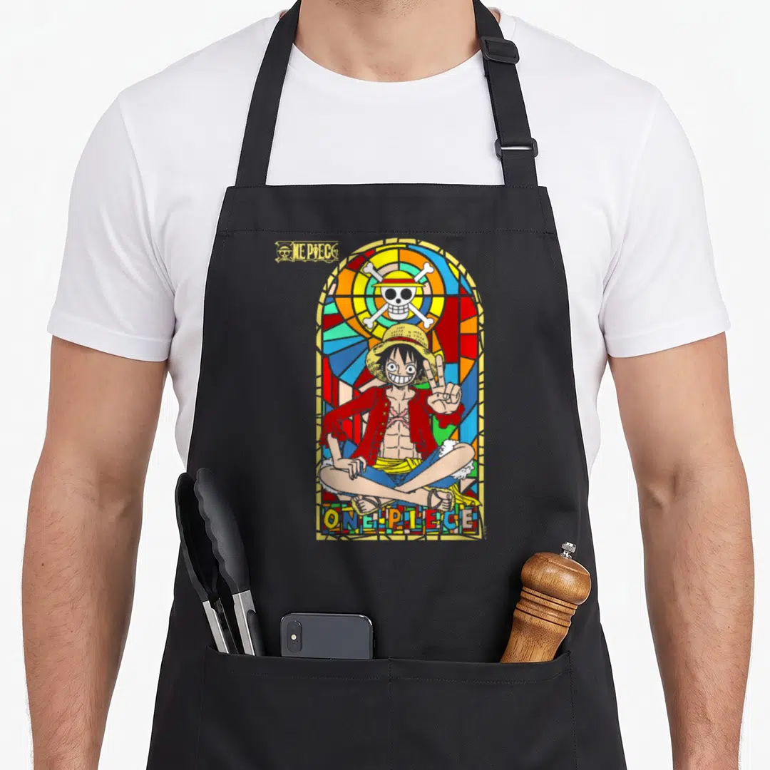 Monkey anime apron - Stained glass ONE PIECE design with Monkey D. Luffy in red yellow blue gold — shown on a black cotton canvas apron against a white background