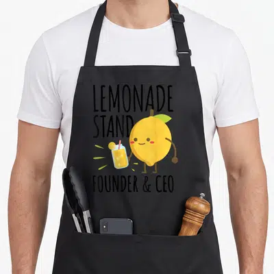 Founder lemonade apron - Cartoon lemon holding drink with LEMONADE STAND FOUNDER CEO text in yellow and black — shown on a black cotton canvas apron against a white background