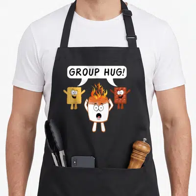 Bonefire camping apron - Cartoon marshmallow on fire with graham cracker and chocolate bar saying group hug — shown on a black cotton canvas apron against a white background