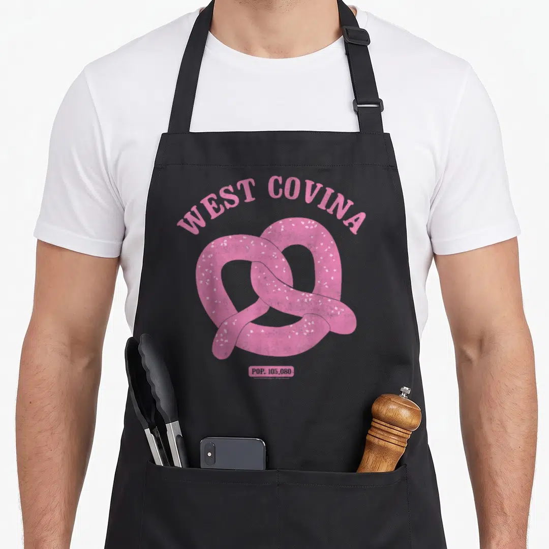 West covina apron - Pink pretzel with white salt specks under arched text reading WEST COVINA and a small box with POP — shown on a black cotton canvas apron against a white background