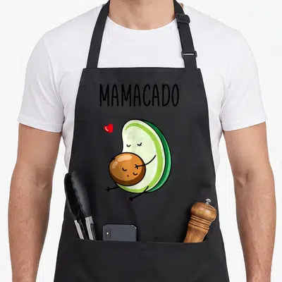 Avo avocado apron - MAMACADO text above cartoon avocado hugging pit with red heart — shown on a black cotton canvas apron against a white background