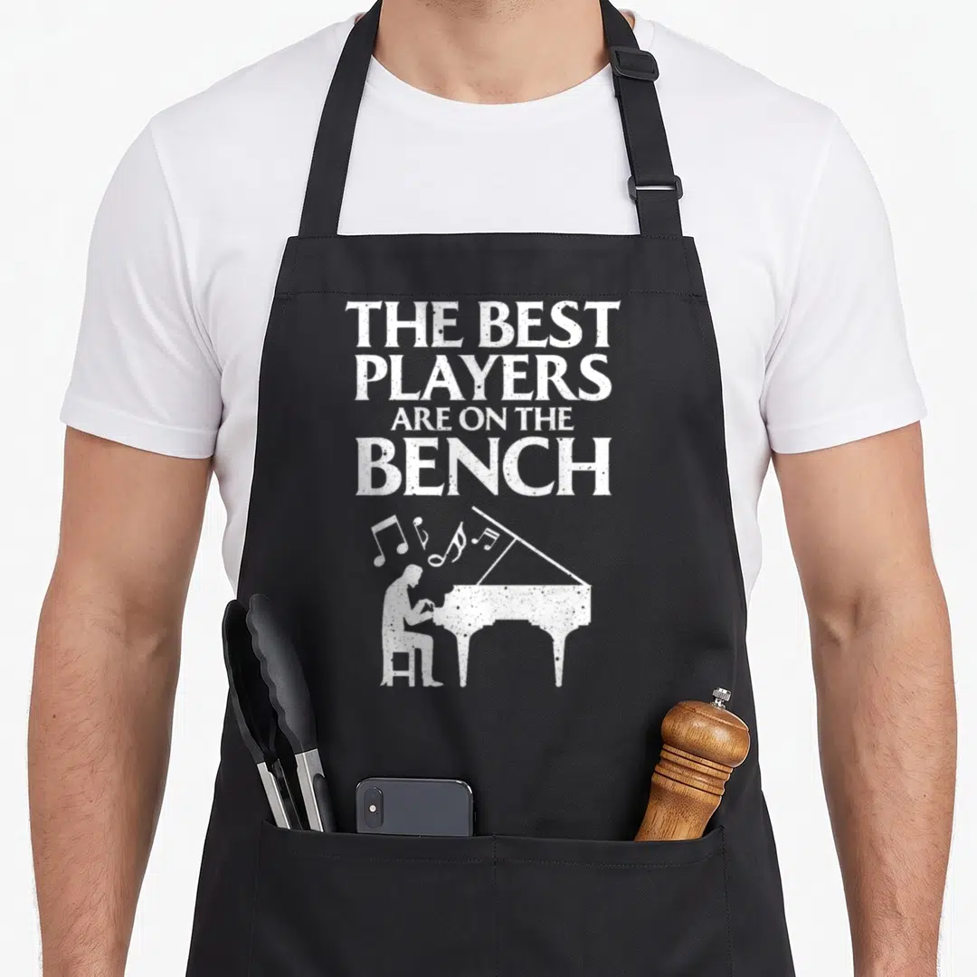 Keyboard player piano apron - Distressed white text and silhouette of person playing grand piano with floating musical — shown on a black cotton canvas apron against a white background