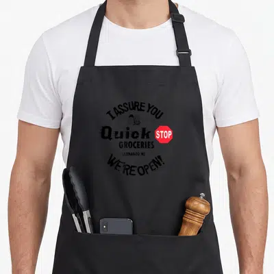 Jay quick apron - Circular Quick Stop sign print with I Assure You We're Open text and red stop sign — shown on a black cotton canvas apron against a white background