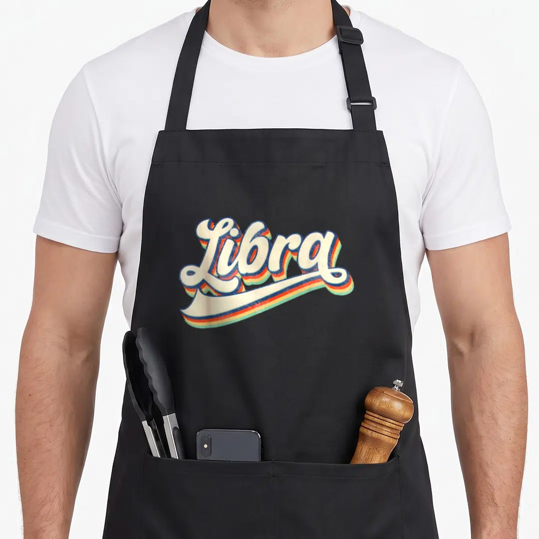 Zodiac september birthday apron - Retro script text Libra with cream orange blue and green shadows — shown on a black cotton canvas apron against a white background