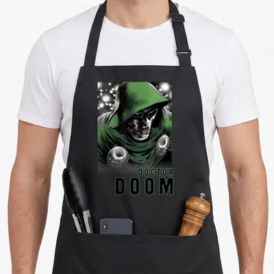 Four doctor apron - Centered Doctor Doom portrait in green and silver with DOCTOR DOOM text below — shown on a black cotton canvas apron against a white background
