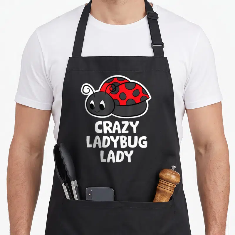 Animal ladybug apron - Cartoon ladybug with red wings and white text reading CRAZY LADYBUG LADY — shown on a black cotton canvas apron against a white background