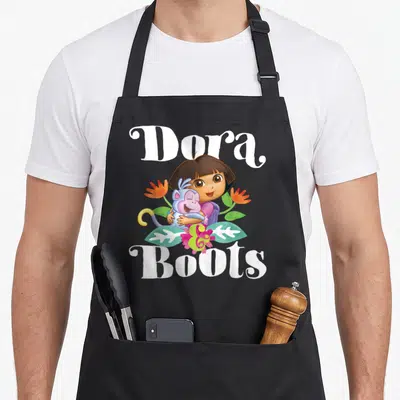 Boot explorer apron - Dora hugging Boots surrounded by green leaves and purple flowers with white text — shown on a black cotton canvas apron against a white background