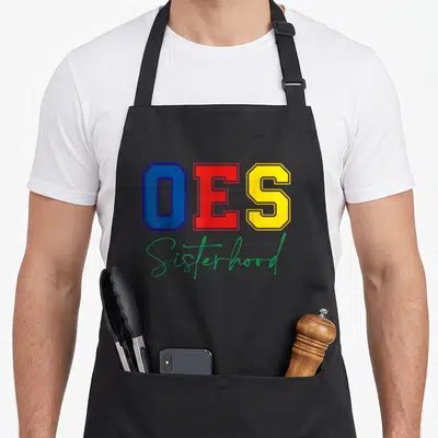 Sisterhood christmas apron - OES in blue red and yellow block letters above green Sisterhood script on black — shown on a black cotton canvas apron against a white background