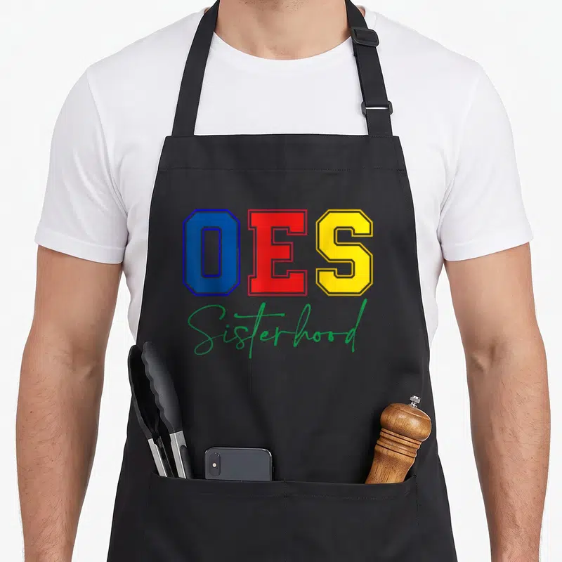 Sisterhood christmas apron - OES in blue red and yellow block letters above green Sisterhood script on black — shown on a black cotton canvas apron against a white background
