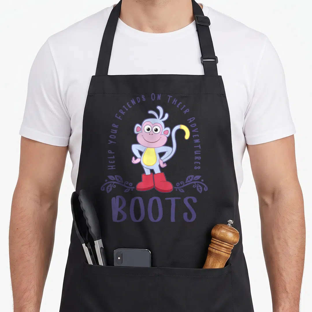 Dora friends apron - Cartoon monkey in red boots with purple text HELP YOUR FRIENDS ON THEIR ADVENTURES BOOTS — shown on a black cotton canvas apron against a white background