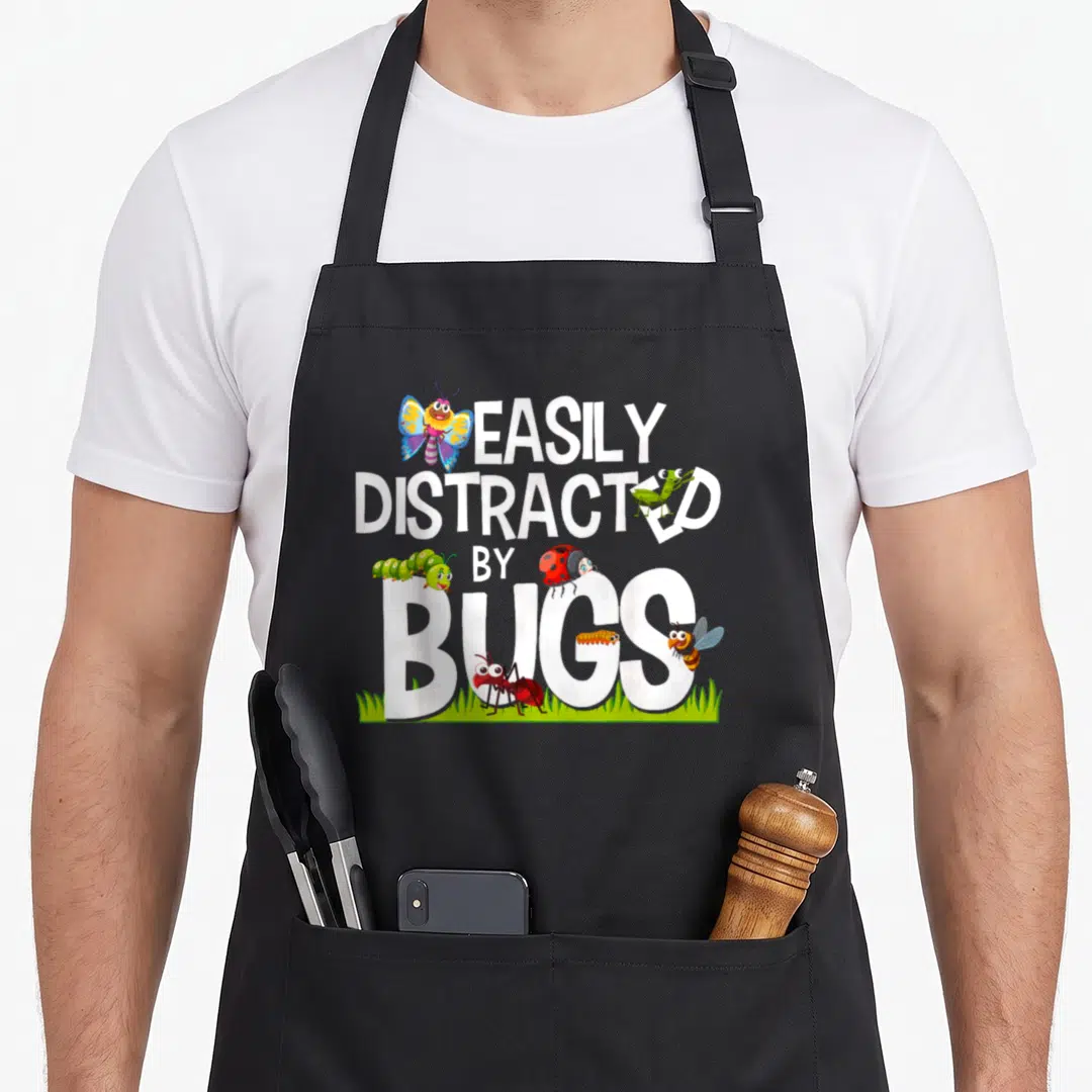 Bug science apron - Cartoon bugs and grass surrounding white text EASILY DISTRACTED BY BUGS — shown on a black cotton canvas apron against a white background