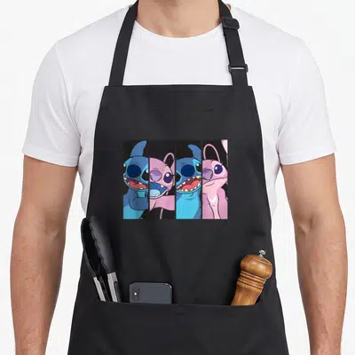 Boxed stitch apron - Four vertical panels of blue and pink cartoon characters smiling against black backgrounds — shown on a black cotton canvas apron against a white background