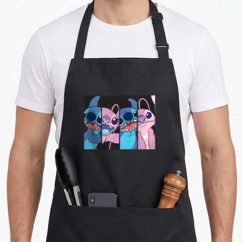 Boxed stitch apron - Four vertical panels of blue and pink cartoon characters smiling against black backgrounds — shown on a black cotton canvas apron against a white background