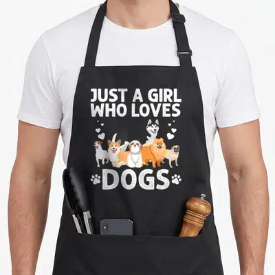 Handler dog groomer apron - Six cartoon dogs between Just a girl who loves dogs text and paw prints — shown on a black cotton canvas apron against a white background