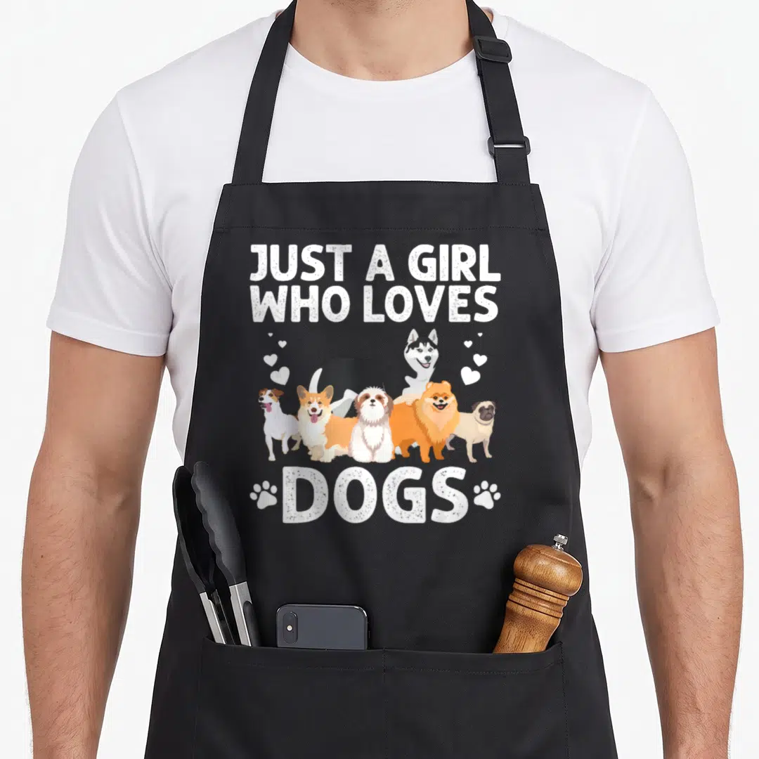 Handler dog groomer apron - Six cartoon dogs between Just a girl who loves dogs text and paw prints — shown on a black cotton canvas apron against a white background