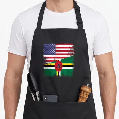Flag dominican pride apron - Distressed split US and Dominica flag design with parrot emblem in red white blue green — shown on a black cotton canvas apron against a white background