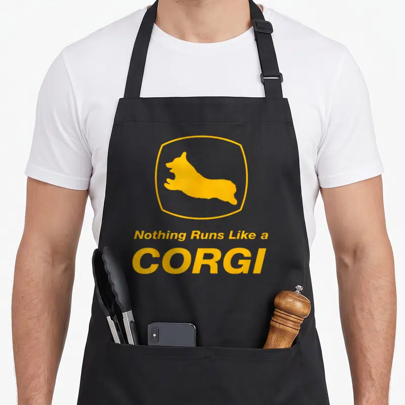 Run corgi apron - Yellow corgi silhouette in hexagon border above stacked text Nothing Runs Like a CORGI — shown on a black cotton canvas apron against a white background