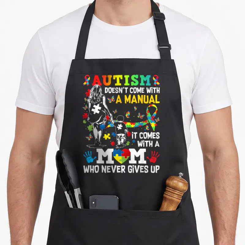 Come autism awareness apron - Mother and child silhouette with rainbow puzzle pieces, ribbon, and stacked text reading — shown on a black cotton canvas apron against a white background