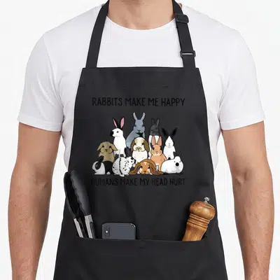 Human rabbit apron - Ten cartoon rabbits in black white grey brown with text RABBITS MAKE ME HAPPY HUMANS MAKE MY HEAD — shown on a black cotton canvas apron against a white background