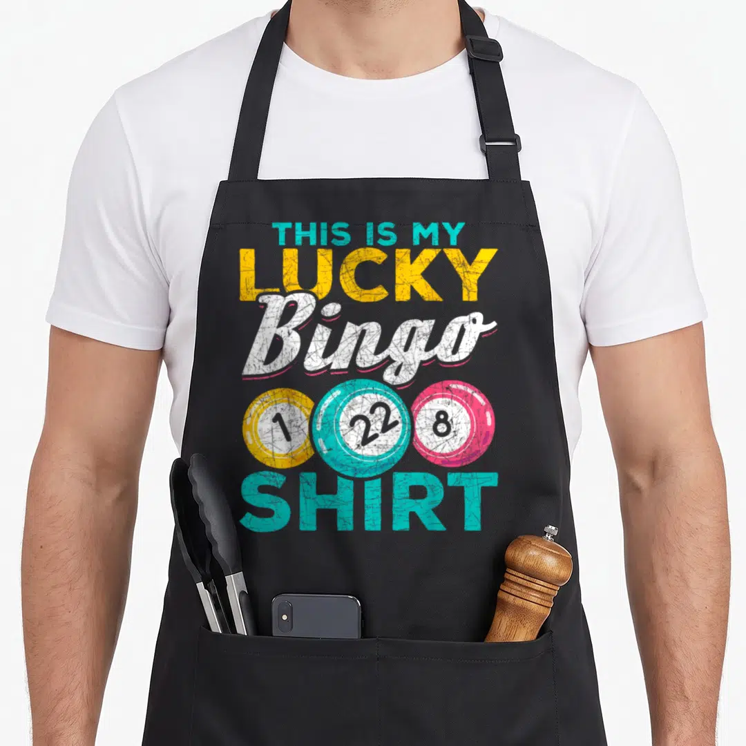 Das bingo apron - Stacked distressed text reading This Is My Lucky Bingo Shirt with three numbered colored balls — shown on a black cotton canvas apron against a white background