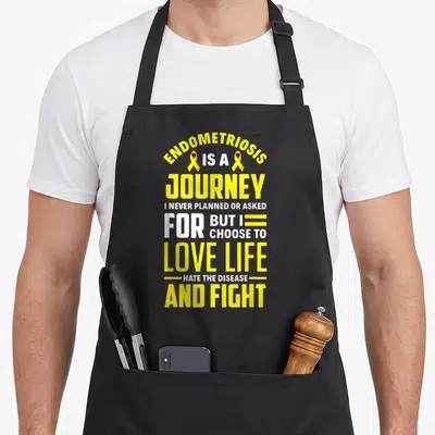 Month endometriosis awareness apron - Yellow and white stacked text design with two ribbons flanking the words Is — shown on a black cotton canvas apron against a white background
