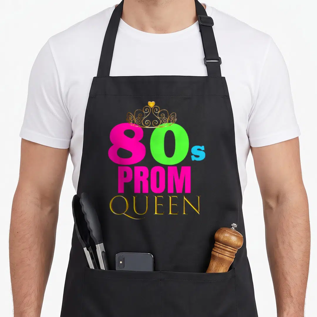 Neon 80s apron - Gold crown over pink 80s PROM QUEEN text with green and blue accents — shown on a black cotton canvas apron against a white background