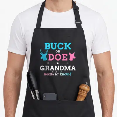 Shower grandma apron - Stacked text BUCK OR DOE GRANDMA needs to know with blue buck and pink doe heads and white star — shown on a black cotton canvas apron against a white background