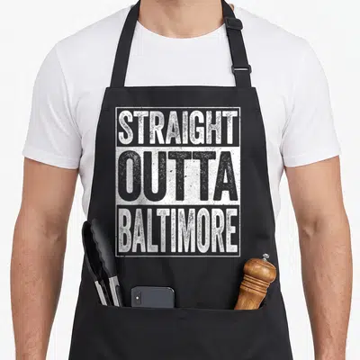 Outta baltimore apron - Stacked white and grey text reading STRAIGHT OUTTA BALTIMORE inside a rectangular border — shown on a black cotton canvas apron against a white background