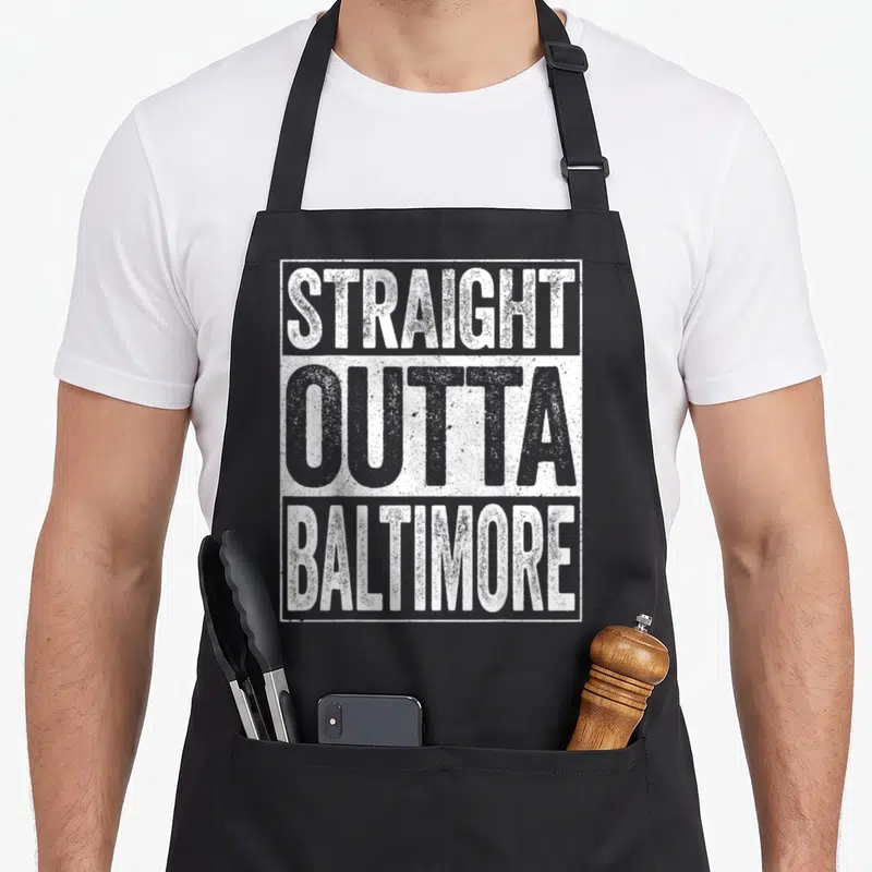 Outta baltimore apron - Stacked white and grey text reading STRAIGHT OUTTA BALTIMORE inside a rectangular border — shown on a black cotton canvas apron against a white background