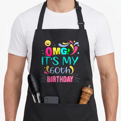 Omg 60th birthday apron - Stacked colorful text reading OMG IT'S MY 60th BIRTHDAY with smiley face and swirls — shown on a black cotton canvas apron against a white background