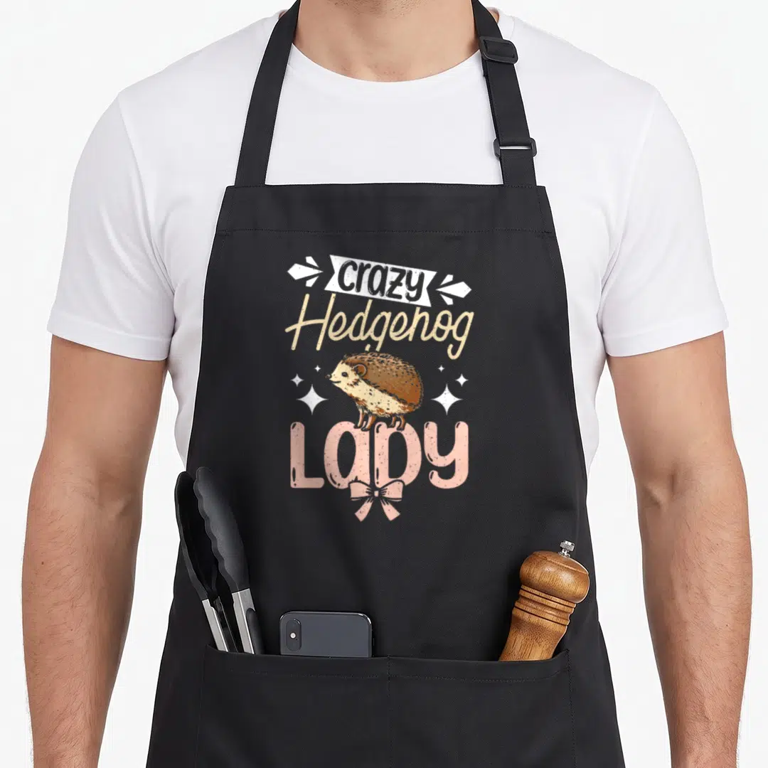 Crazy hedgehog gal apron - Cartoon hedgehog above pink LADY text with white stars and ribbon — shown on a black cotton canvas apron against a white background