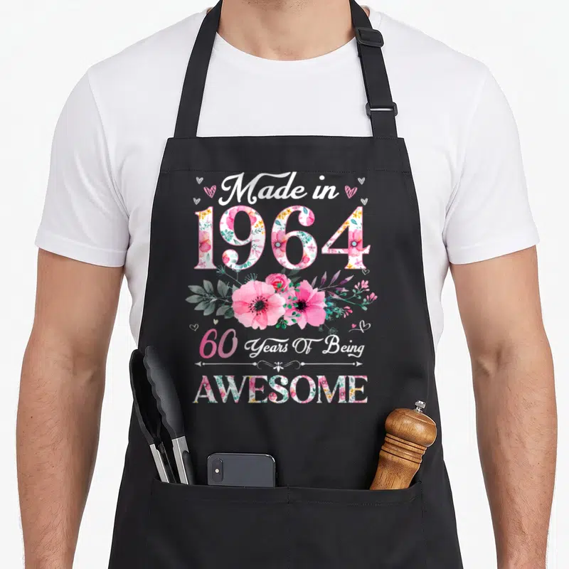60th birthday vintage floral apron - Pink watercolor flowers fill 1964 text with Made in 1964 and 60 Years Of Being — shown on a black cotton canvas apron against a white background