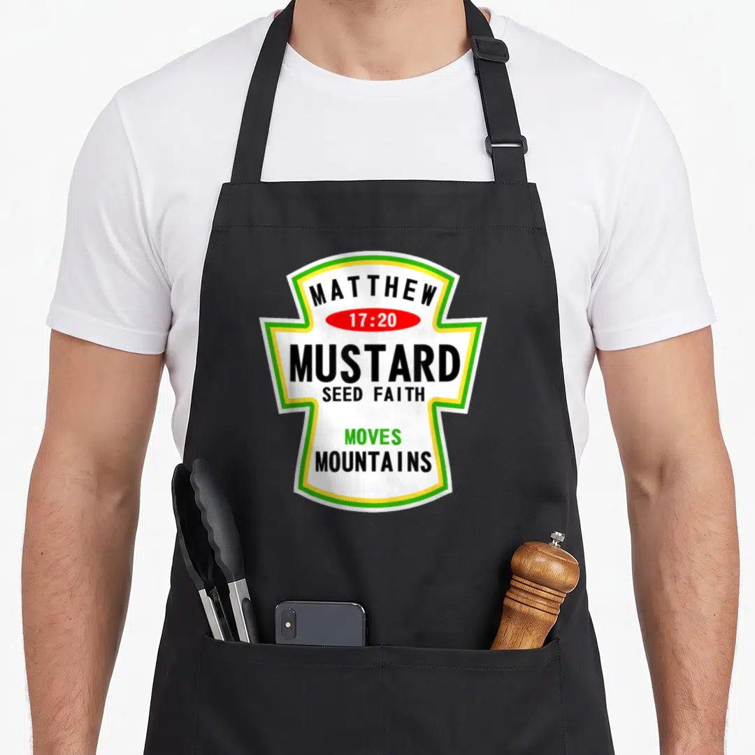 Costume christian apron - Mustard seed faith typography in white label with green yellow border and red oval citation — shown on a black cotton canvas apron against a white background