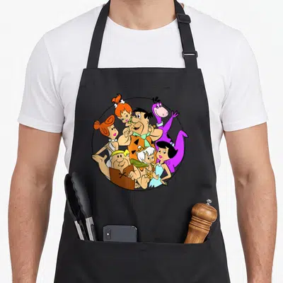 Shot flint apron - Flintstones family clustered in a black circle with orange purple blue and white cartoon art — shown on a black cotton canvas apron against a white background
