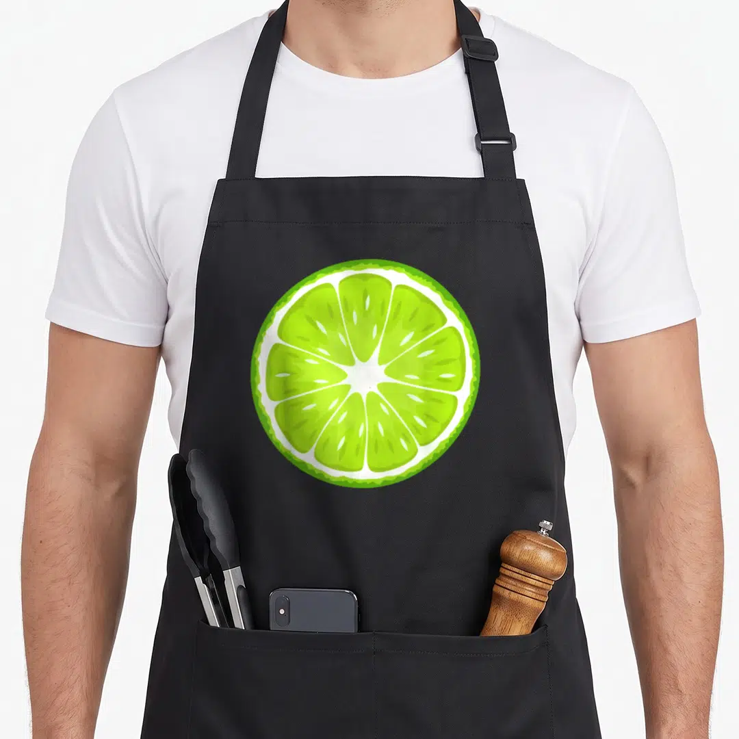 Fruit halloween apron - Cartoon green lime slice centered on white background — shown on a black cotton canvas apron against a white background