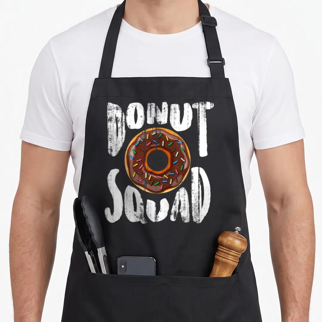 Squad doughnut donut apron - Donut Squad text with chocolate frosted donut and sprinkles center — shown on a black cotton canvas apron against a white background
