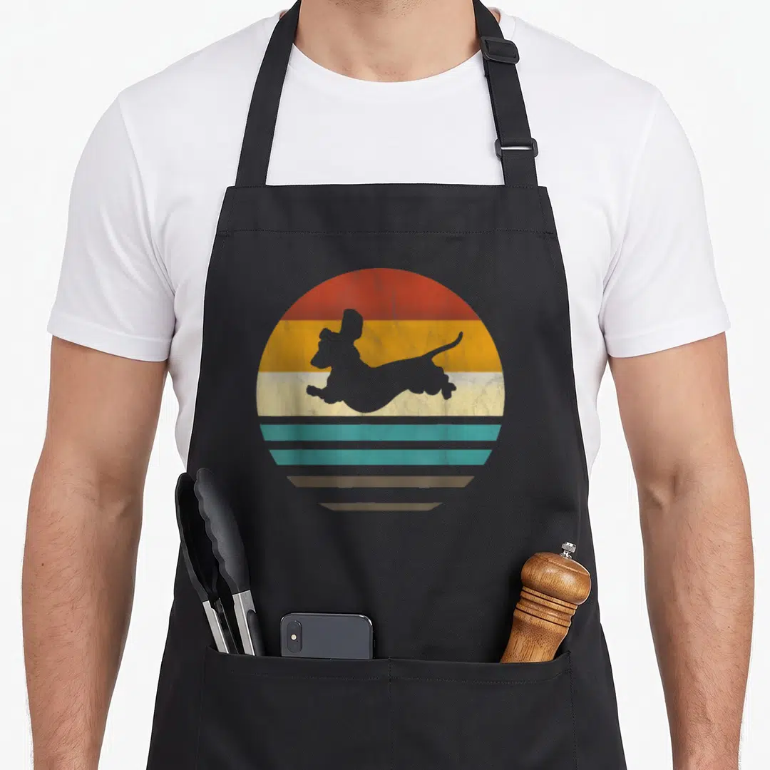 Dachshund dog apron - Grey jumping dog silhouette over retro sun with red orange yellow teal and grey horizontal stripes — shown on a black cotton canvas apron against a white background