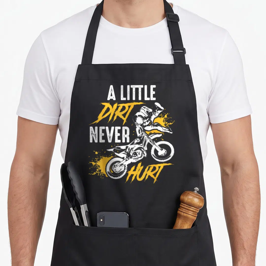 Hurt bike apron - A Little Dirt Never Hurt motocross rider graphic in distressed white and yellow — shown on a black cotton canvas apron against a white background