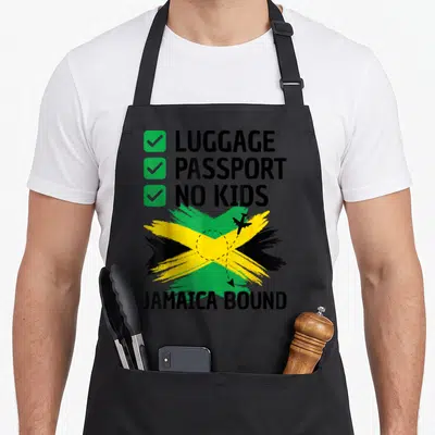 Jamaican travel aprons - Checklist reading Luggage Passport No Kids above brush stroke Jamaican flag with airplane — shown on a black cotton canvas apron against a white background
