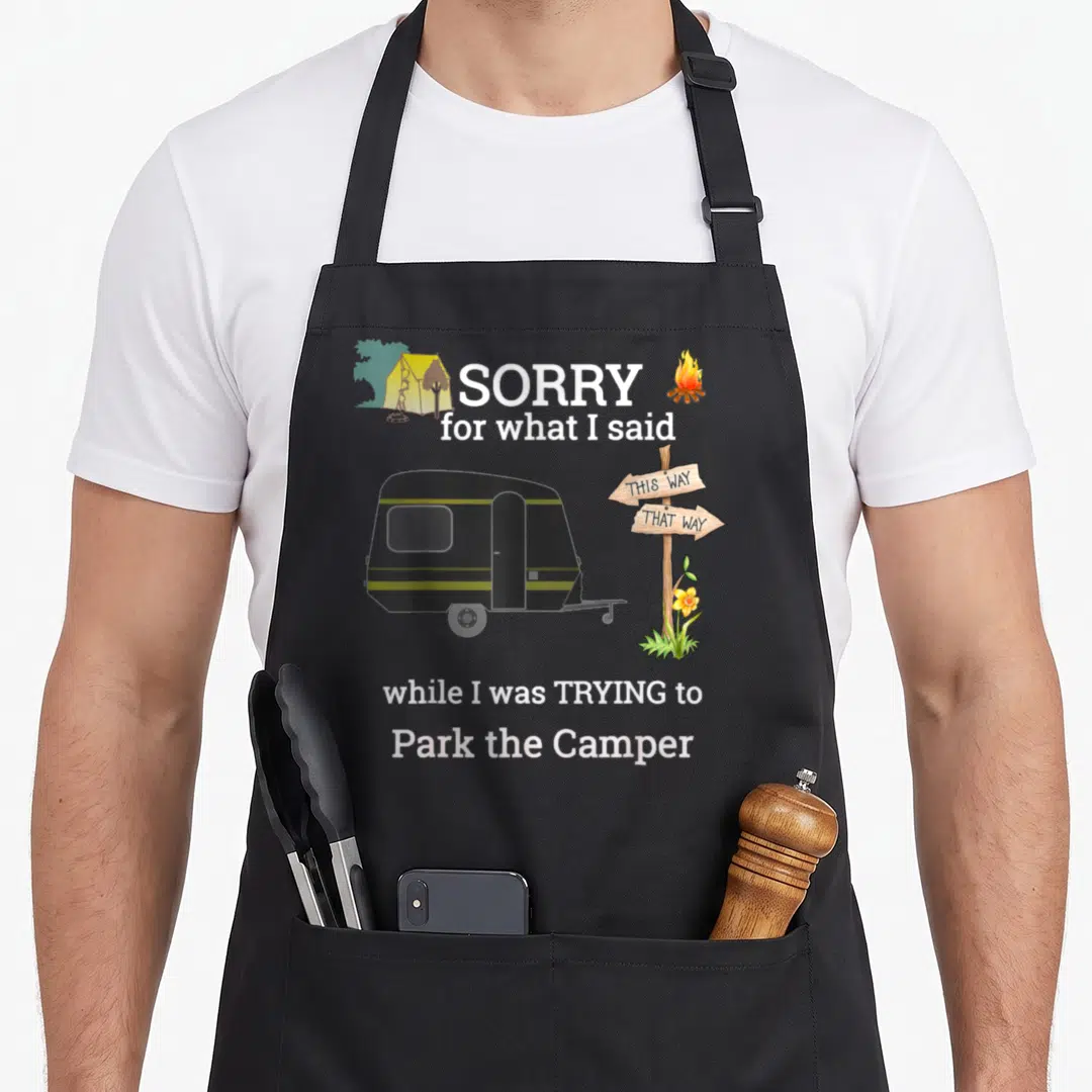 Camper parking apron - Cartoon camper with signpost and text Sorry for what I said while I was TRYING to Park the Camper — shown on a black cotton canvas apron against a white background