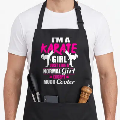 But karate apron - Pink and white text I'M A KARATE GIRL with two white silhouettes of girls doing high kicks — shown on a black cotton canvas apron against a white background