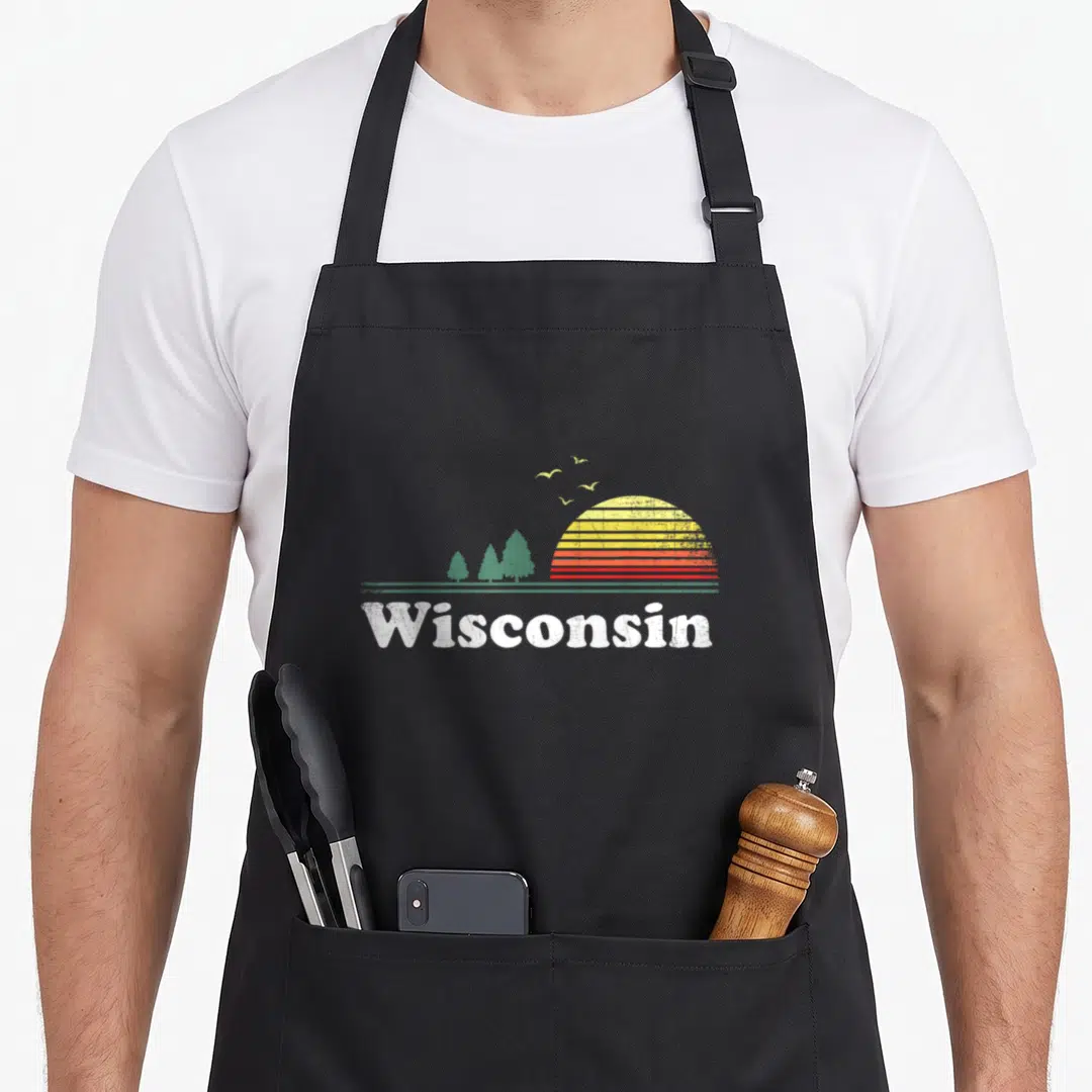 State wisconsin apron - Retro striped sun over green pines with white Wisconsin text — shown on a black cotton canvas apron against a white background