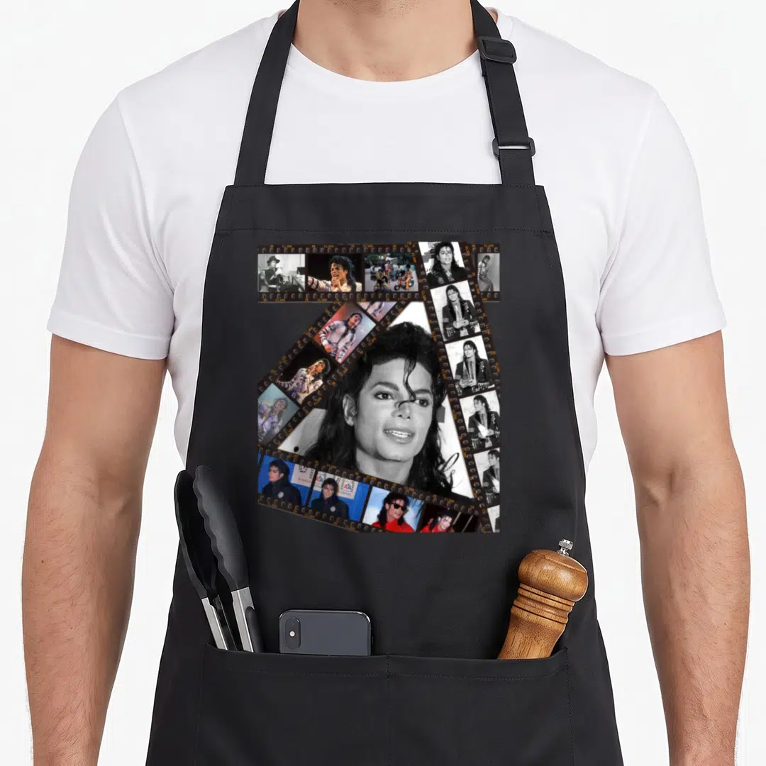 King michaels apron - Michael Jackson central portrait surrounded by film strip collage in black white grey — shown on a black cotton canvas apron against a white background