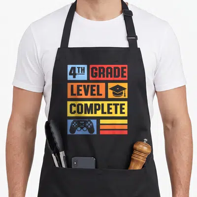 4th grade level apron - Game controller and graduation cap in colored blocks with 4th grade level complete text — shown on a black cotton canvas apron against a white background