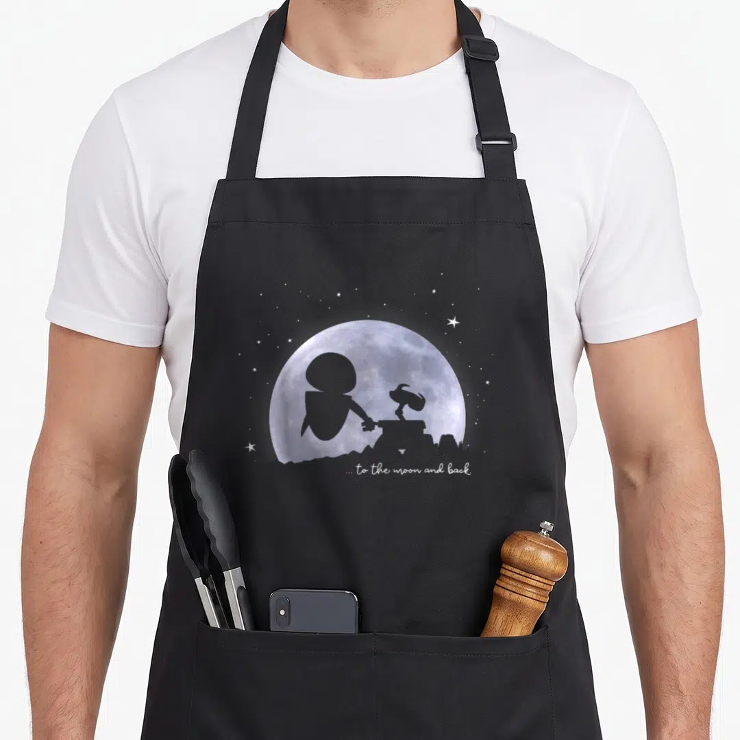 Moon e.a apron - Purple watercolor moon with grey astronaut and rover silhouettes and white text ... to the moon — shown on a black cotton canvas apron against a white background